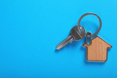 Key with trinket in shape of house on blue background, top view and space for text. Real estate agent services