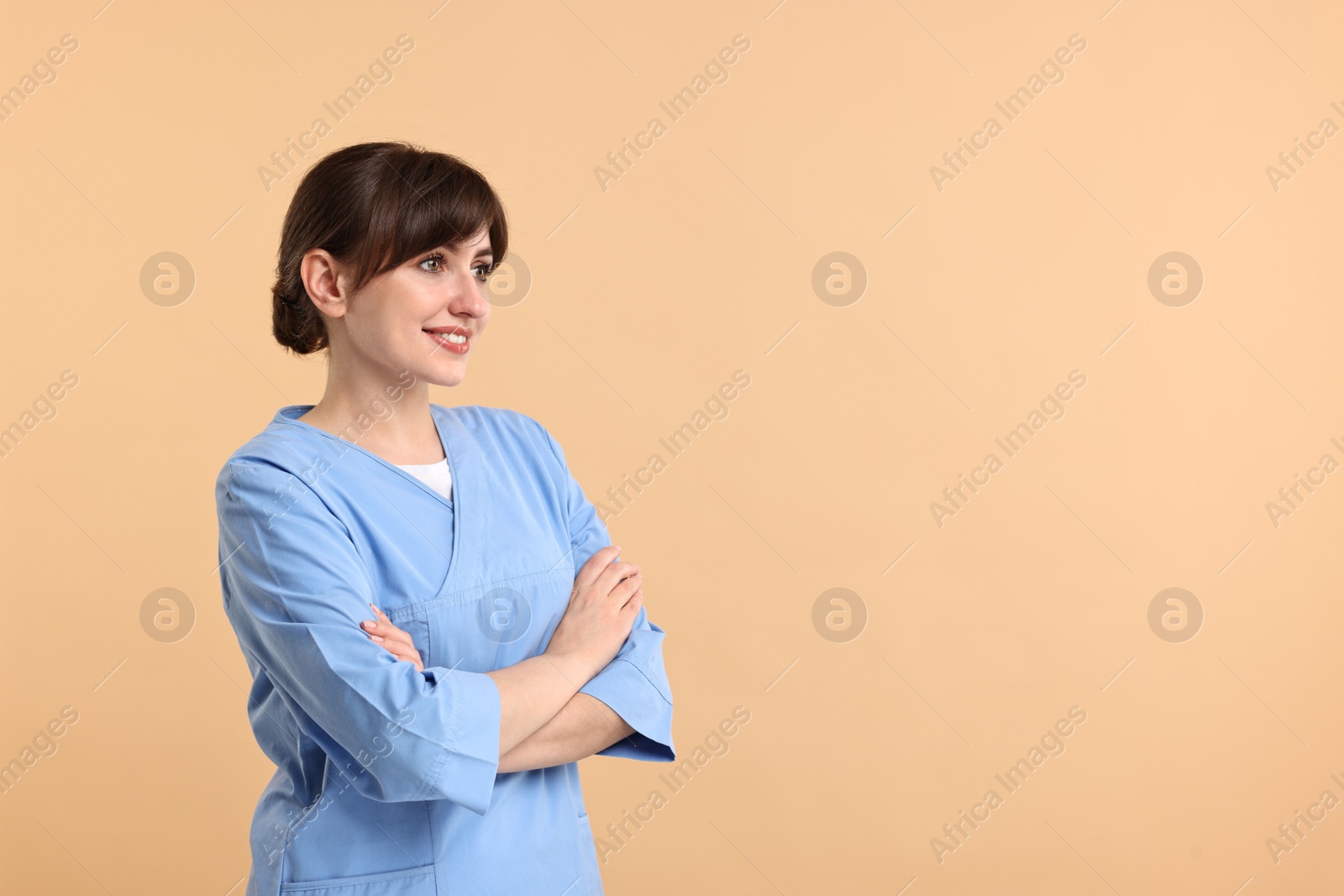 Photo of Portrait of smiling medical assistant with crossed arms on beige background. Space for text