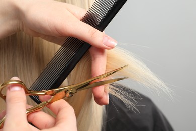 Hairdresser cutting client's hair with scissors on light grey background, closeup