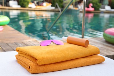 Beach towels, sunglasses and sunscreen on sun lounger near outdoor swimming pool, selective focus. Luxury resort