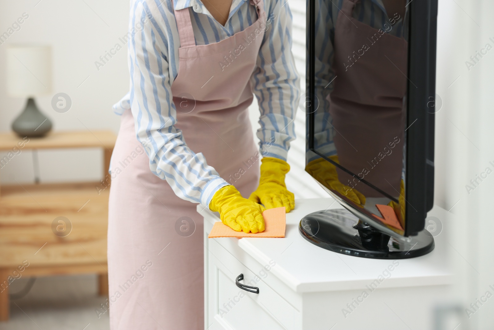 Photo of Young chambermaid wiping dust from furniture in hotel room, closeup