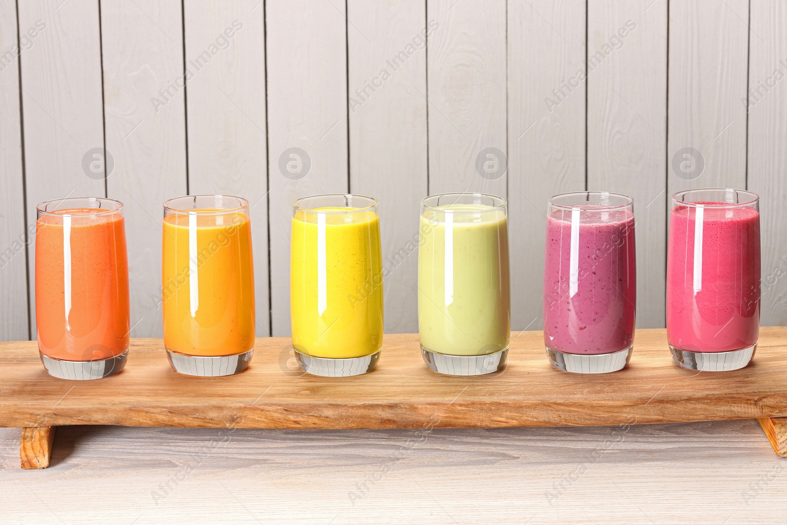 Photo of Board with many different tasty smoothies against white wooden background, space for text