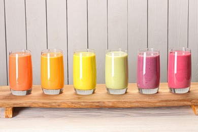 Photo of Board with many different tasty smoothies against white wooden background, space for text