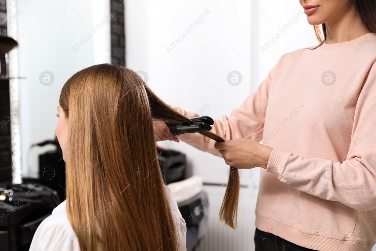 Photo of Hairdresser using straightener to style client's hair in salon