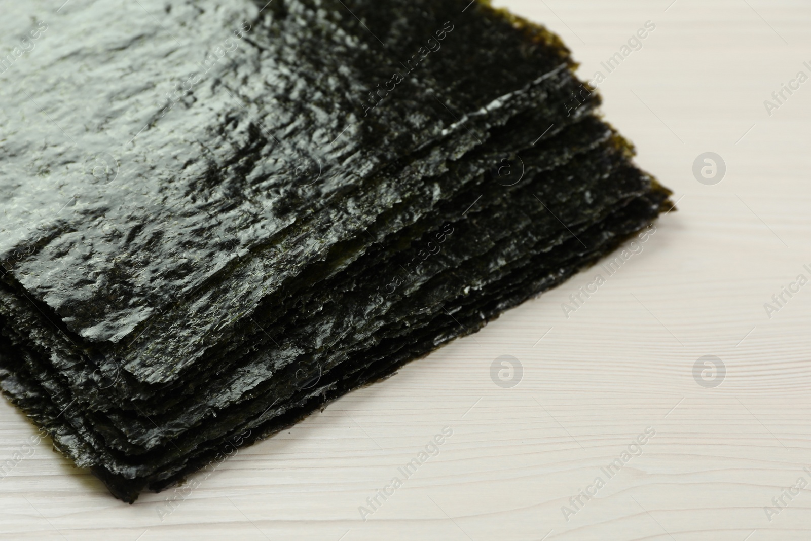 Photo of Stack of dry nori sheets on white wooden table, closeup. Space for text