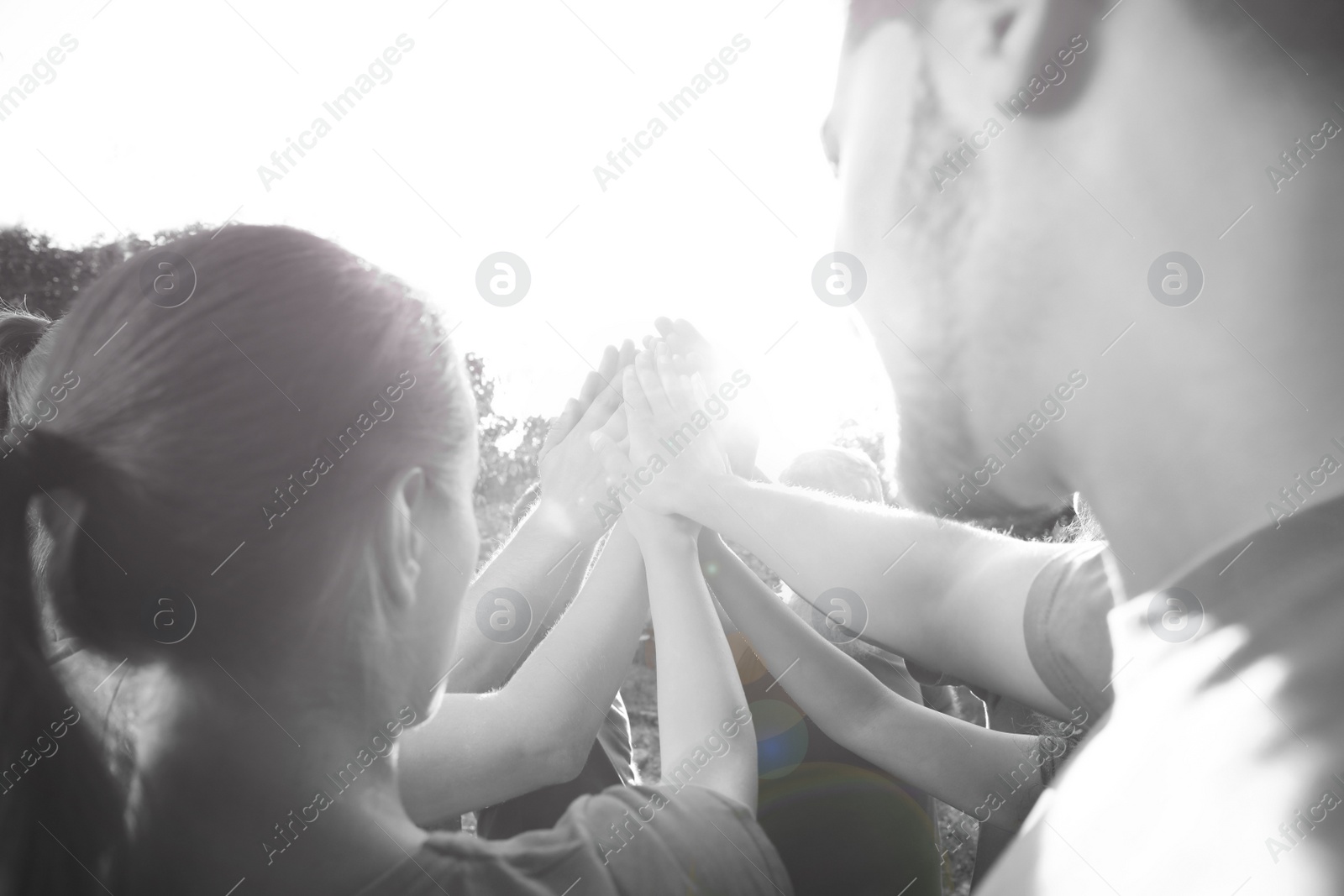 Image of Group of volunteers joining hands together outdoors. Black and white effect