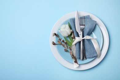 Photo of Festive table setting with willow twigs and tulip on light blue background, top view with space for text. Easter celebration