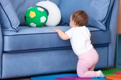 Cute baby holding on to couch in living room. Learning to walk