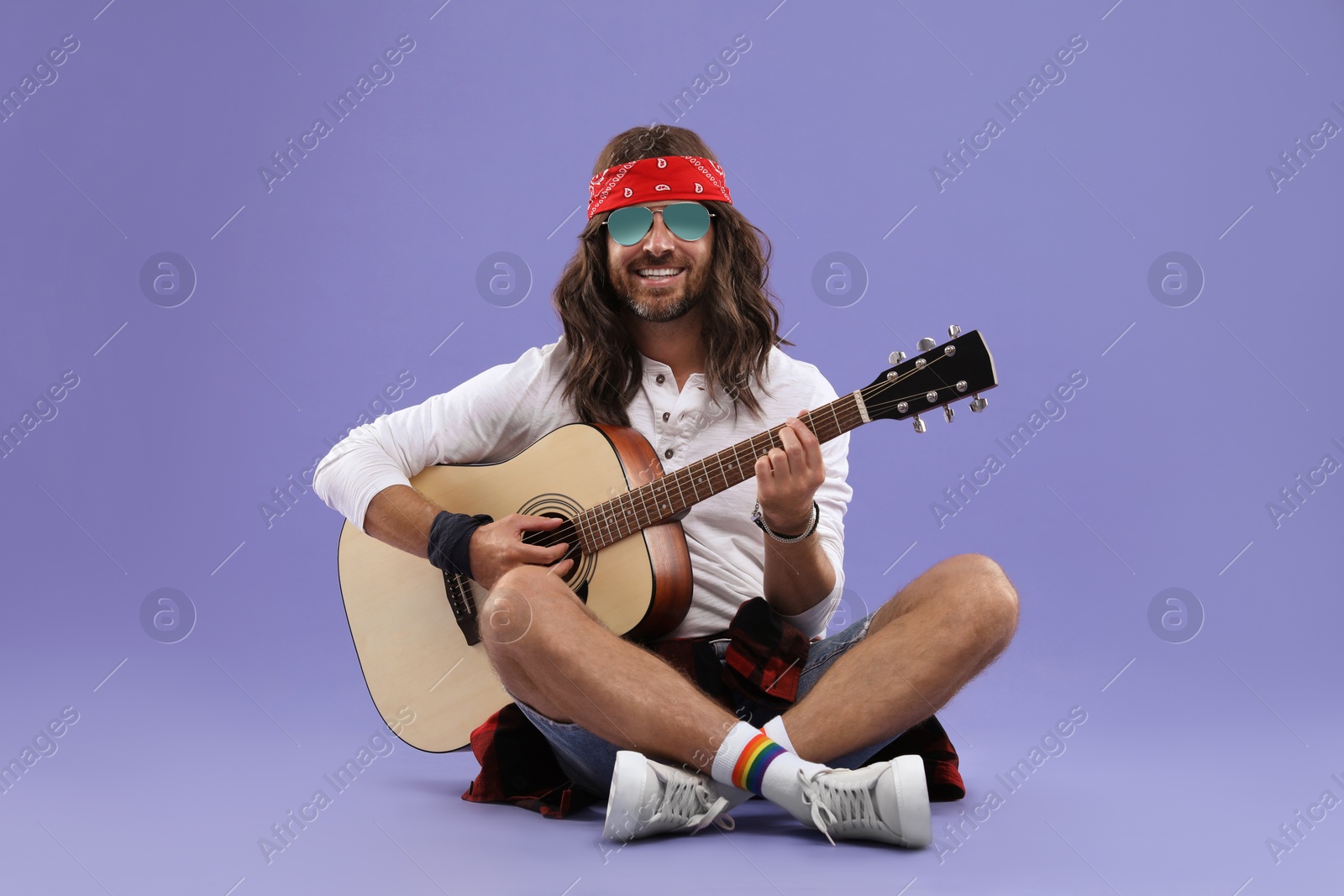 Photo of Stylish hippie man in sunglasses playing guitar on violet background