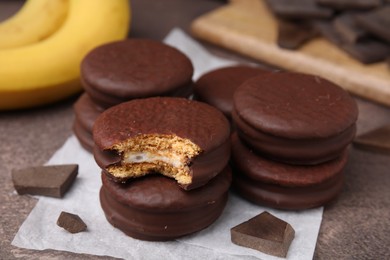 Photo of Tasty banana choco pies and pieces of chocolate on textured table, closeup