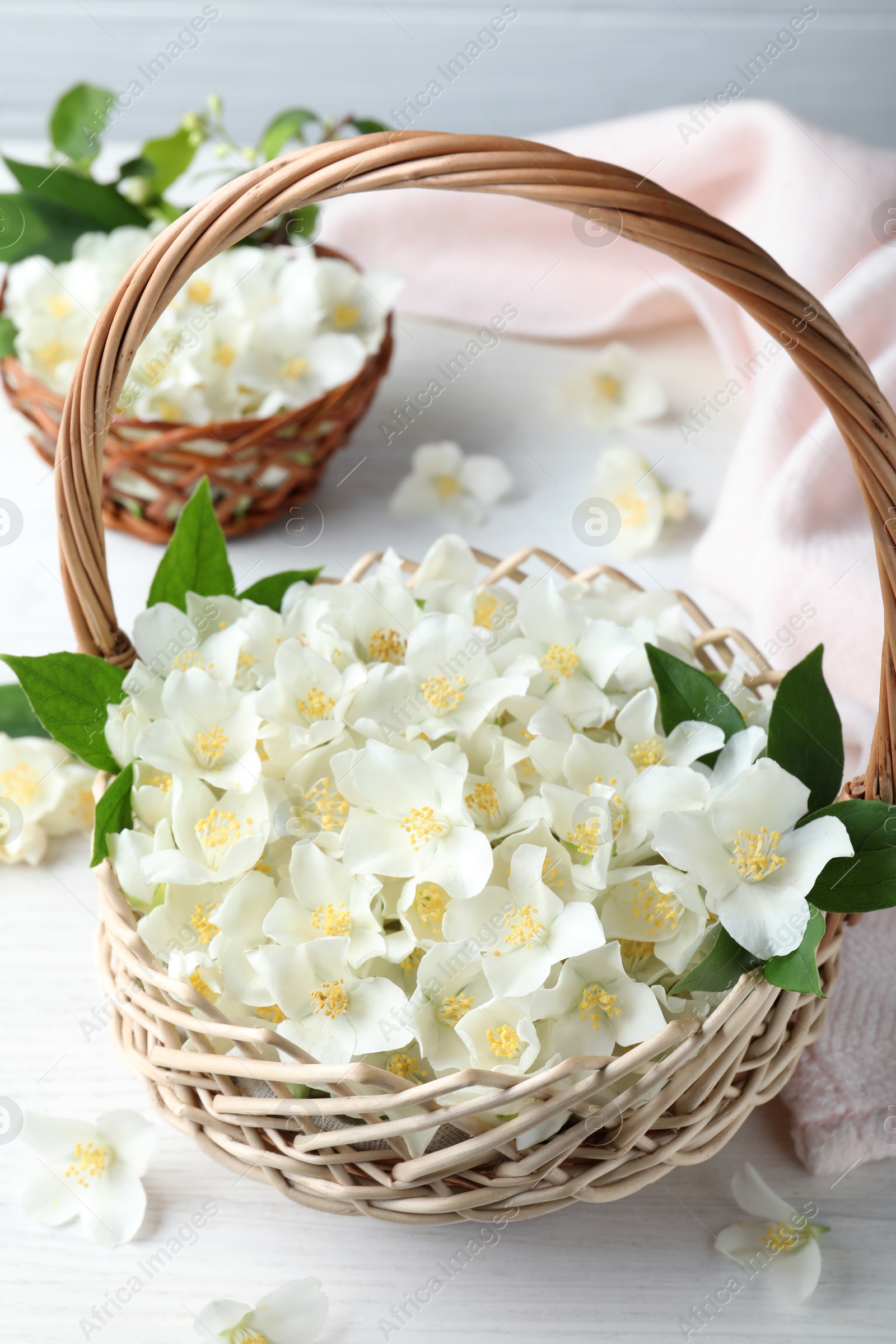 Photo of Beautiful jasmine flowers in wicker basket on white wooden table