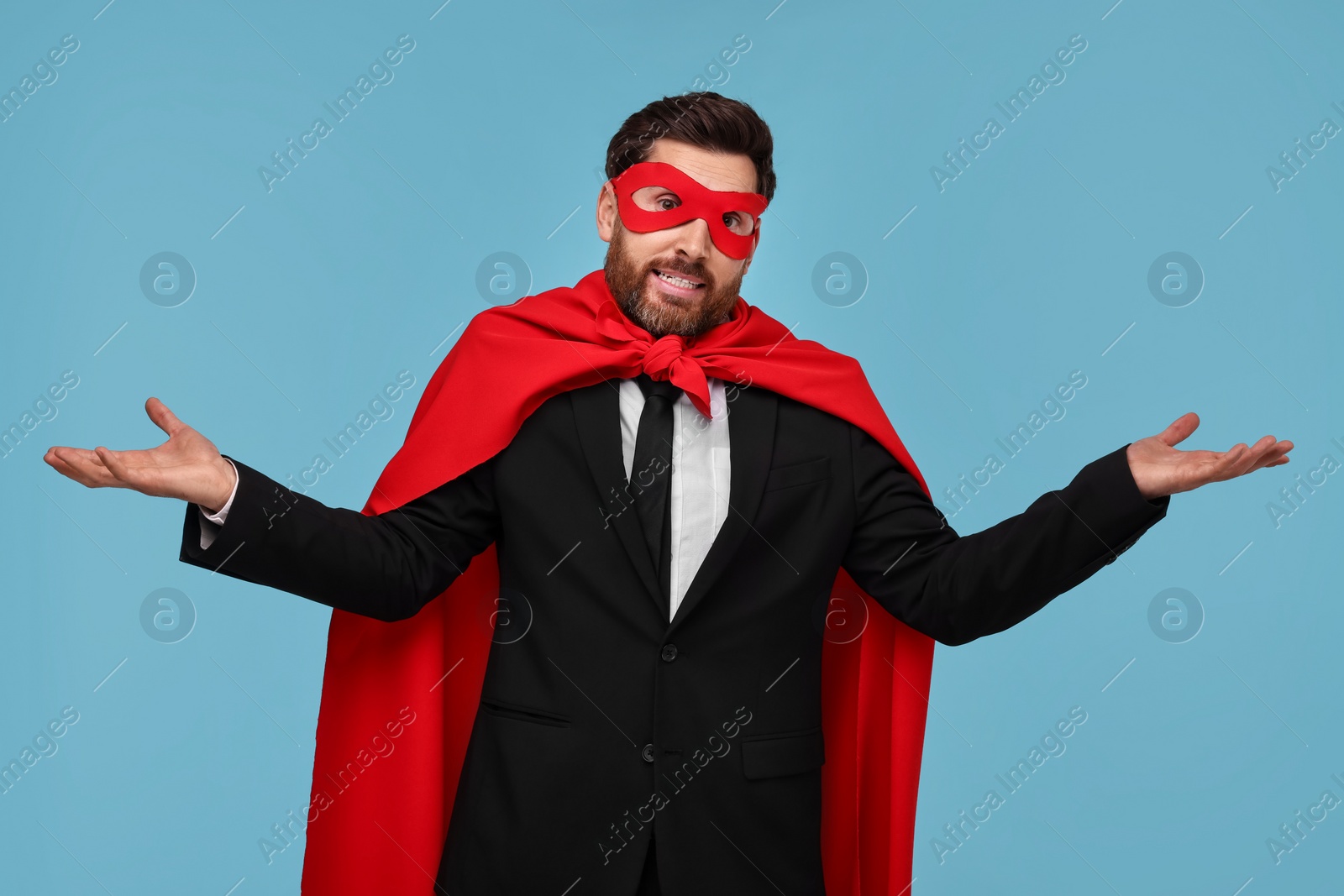 Photo of Businessman wearing red superhero cape and mask on light blue background