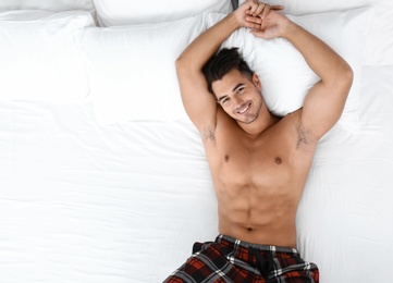 Photo of Sexy young man lying on bed with soft pillows at home, top view