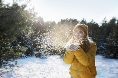 Photo of Woman blowing snow from hands in winter forest, space for text