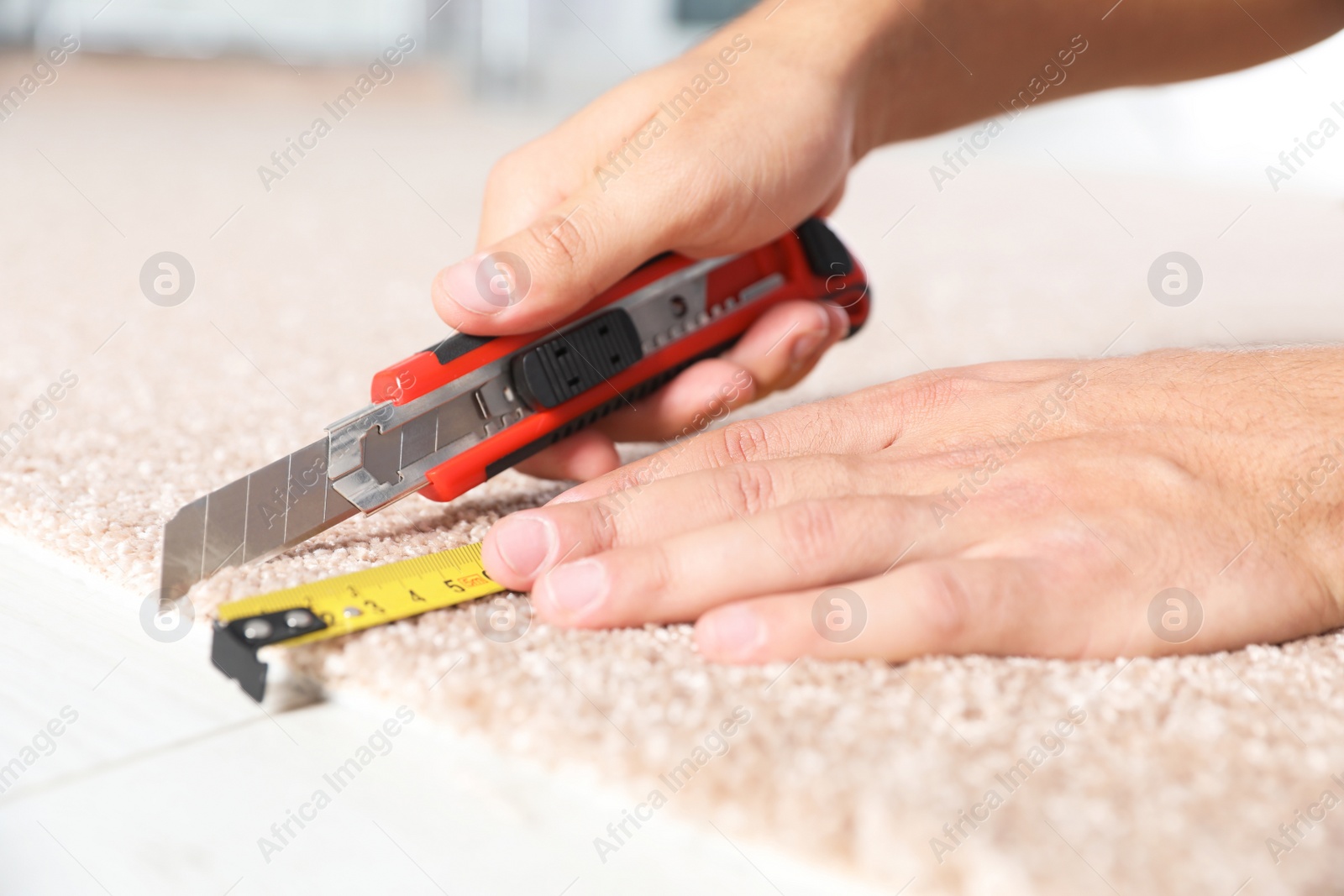 Photo of Man cutting new carpet flooring indoors, closeup