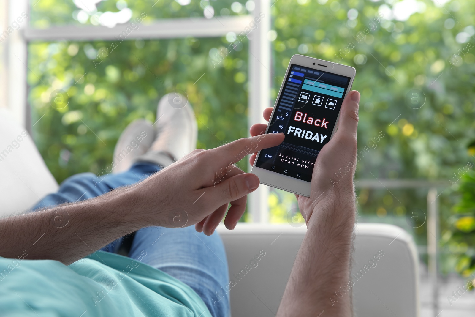 Photo of Man shopping online using smartphone on couch at home, closeup. Black Friday Sale