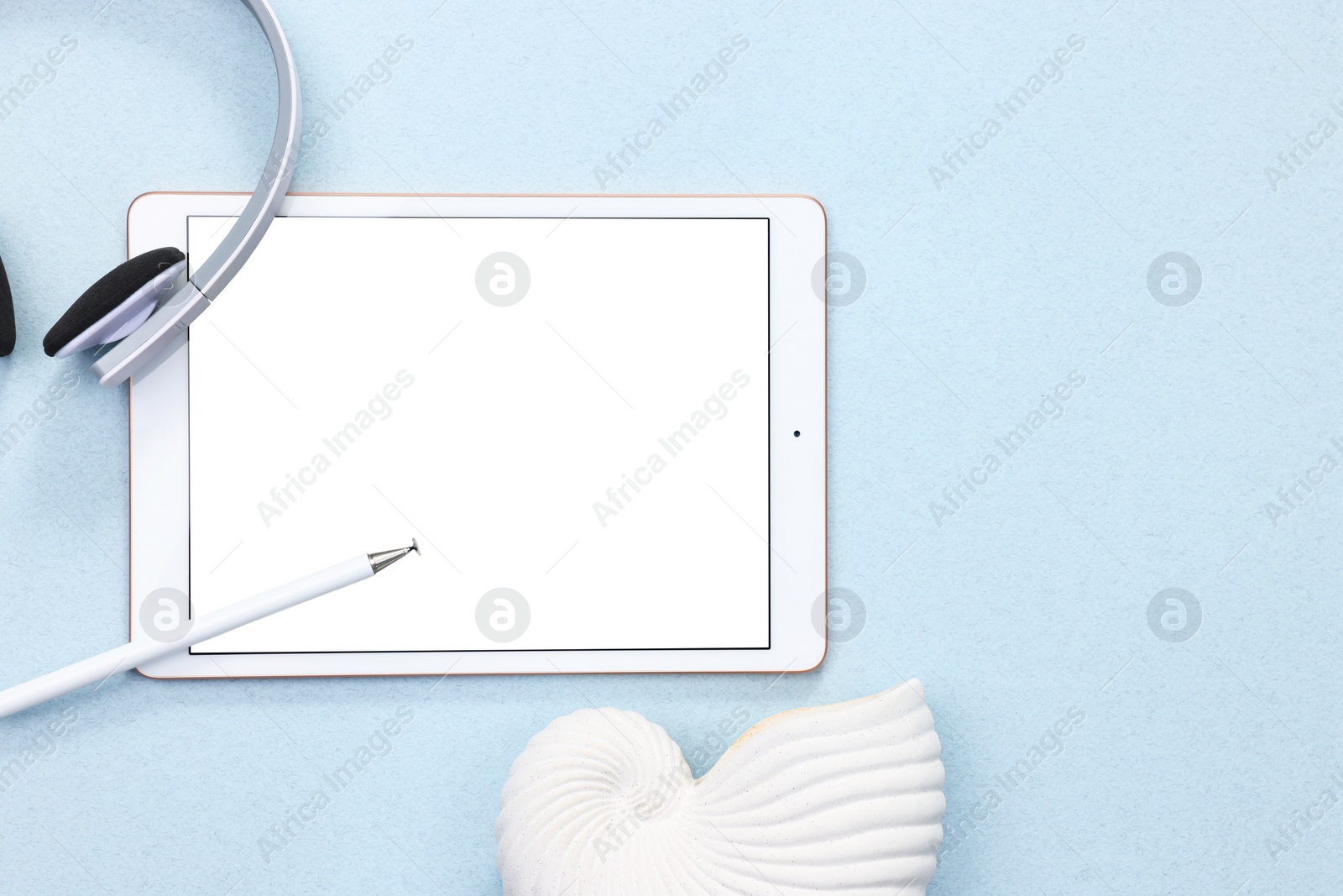 Photo of Modern tablet, headphones and sea shell on light background, flat lay. Space for text