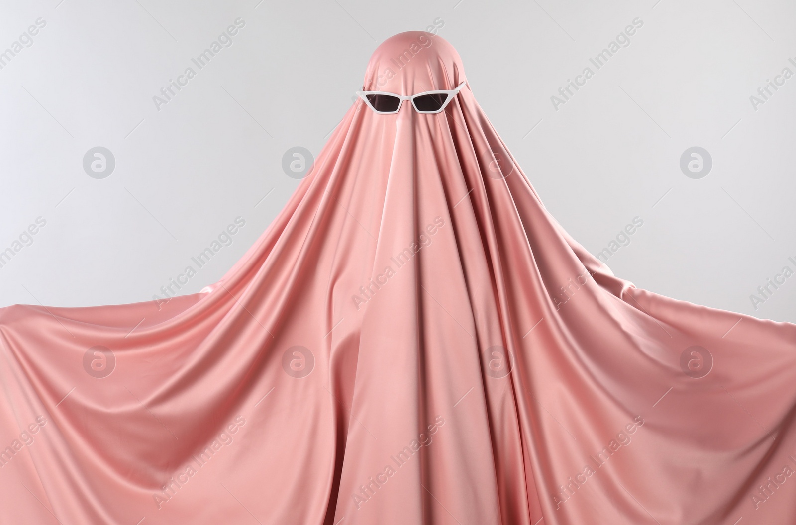 Photo of Glamorous ghost. Woman in pink sheet with sunglasses on light grey background