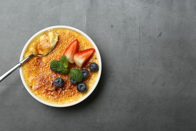 Delicious creme brulee with berries and mint in bowl on grey table, top view. Space for text