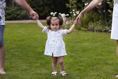 Photo of Parents supporting baby girl while she learning to walk on green grass in park