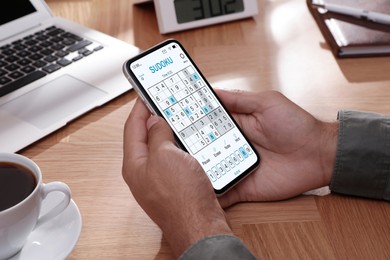 Image of Man playing sudoku game on smartphone indoors, closeup