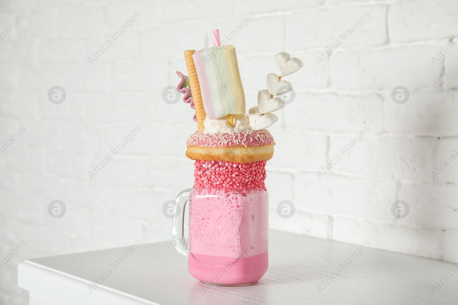 Photo of Tasty milk shake with sweets in mason jar on table near brick wall