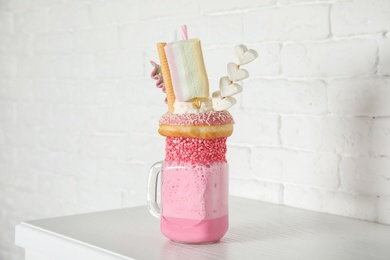 Photo of Tasty milk shake with sweets in mason jar on table near brick wall