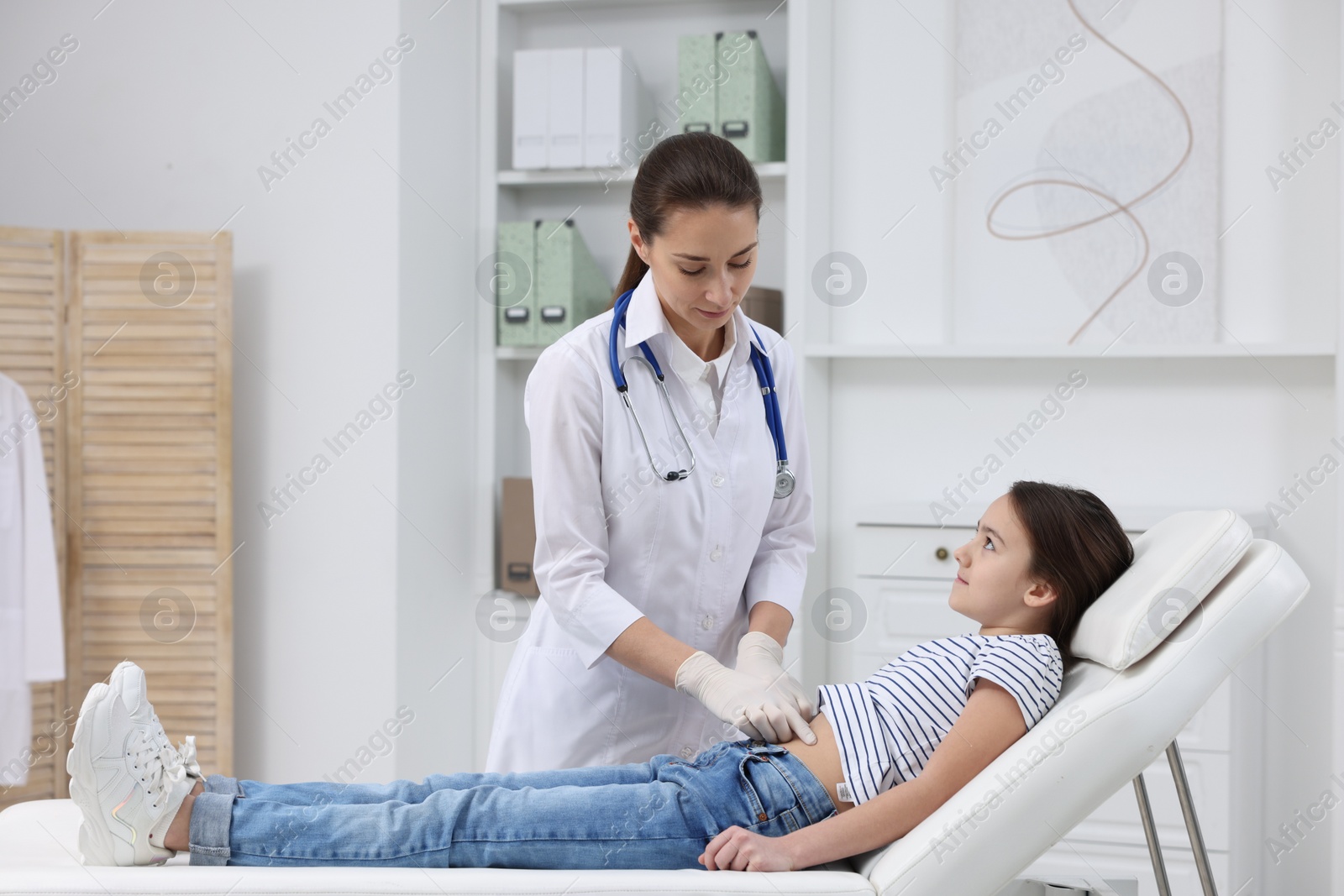 Photo of Gastroenterologist examining girl with stomach ache on couch in clinic