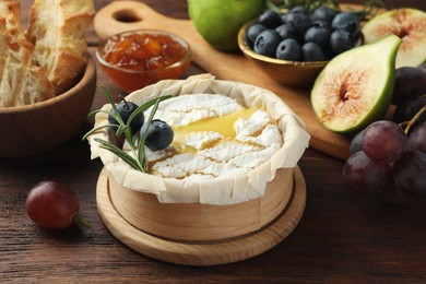 Photo of Tasty baked brie cheese and products on wooden table