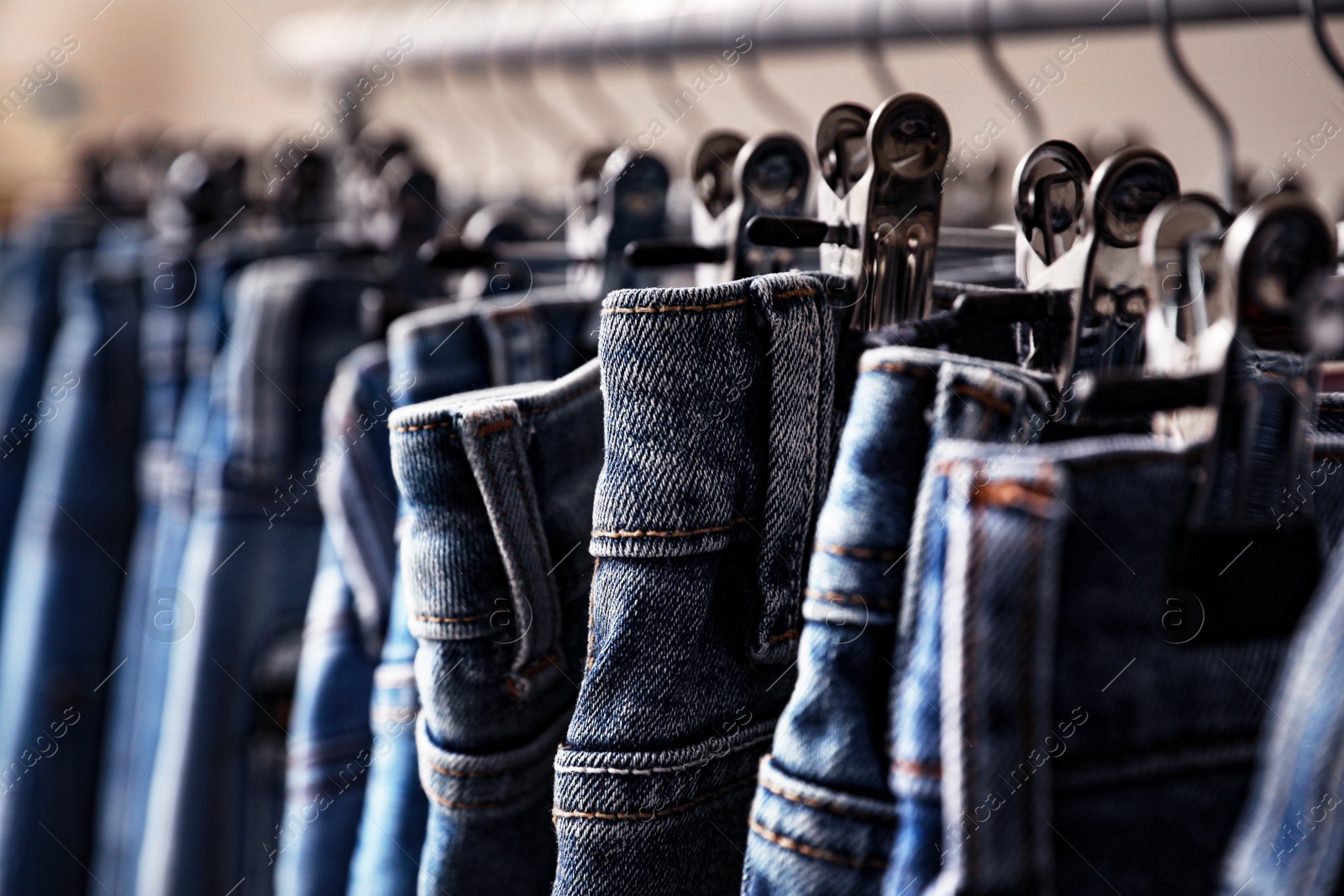 Photo of Hangers with stylish jeans on beige background, closeup