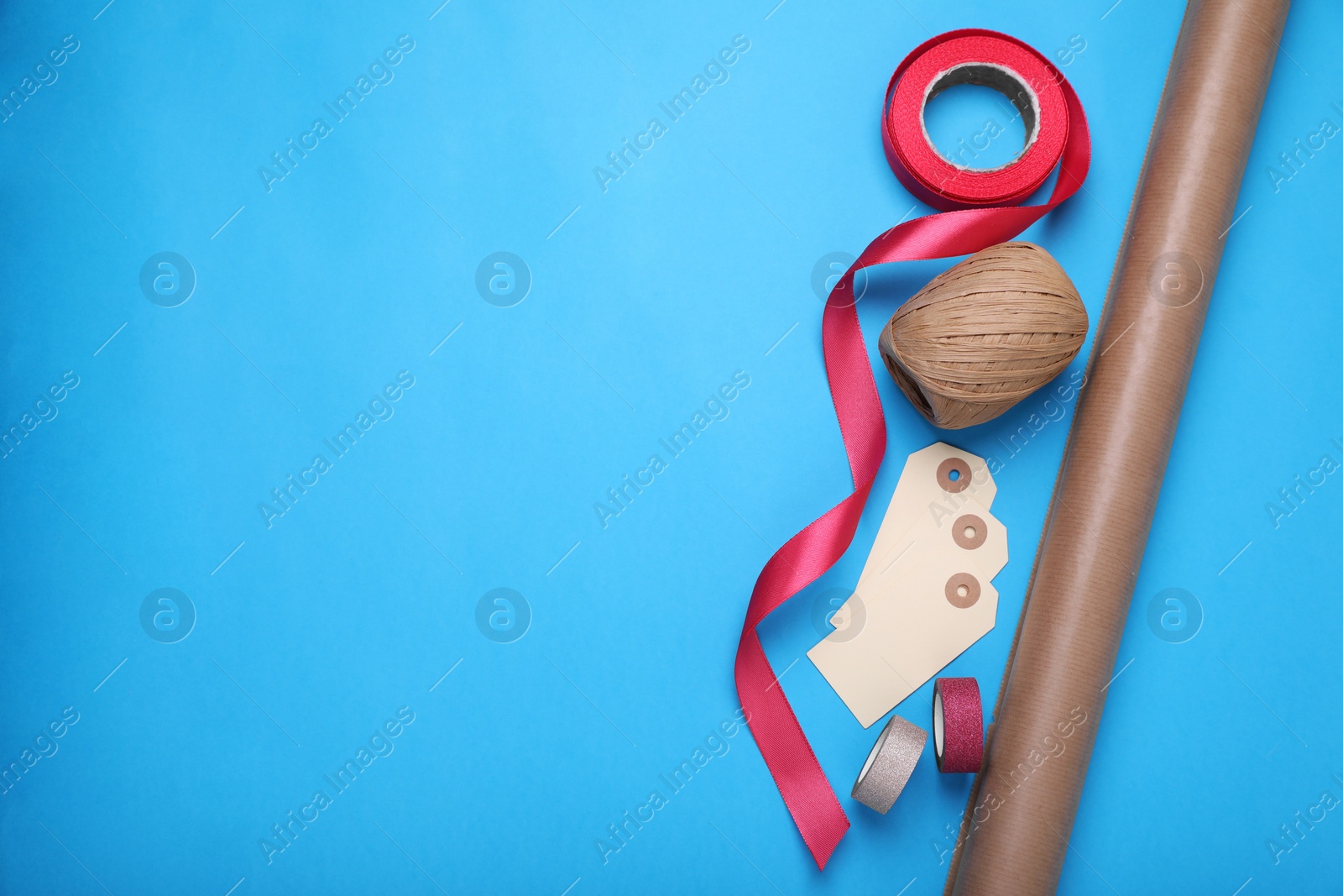 Photo of Roll of wrapping paper, tags and ribbons on light blue background, flat lay. Space for text