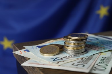 Photo of Coins and banknotes on wooden table against European Union flag, closeup. Space for text