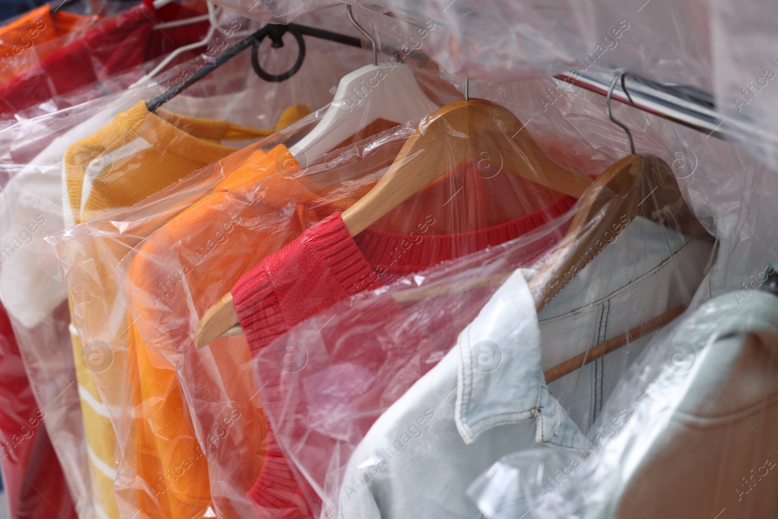 Photo of Dry-cleaning service. Hangers with different clothes in plastic bags on rack, closeup