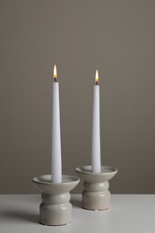 Photo of Holders with burning candles on white table near pale brown wall