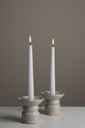 Holders with burning candles on white table near pale brown wall