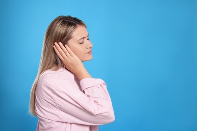 Young woman suffering from ear pain on light blue background. Space for text