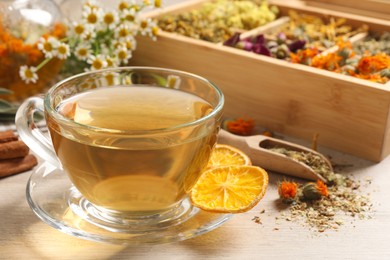 Photo of Freshly brewed tea and dried herbs on white wooden table, closeup