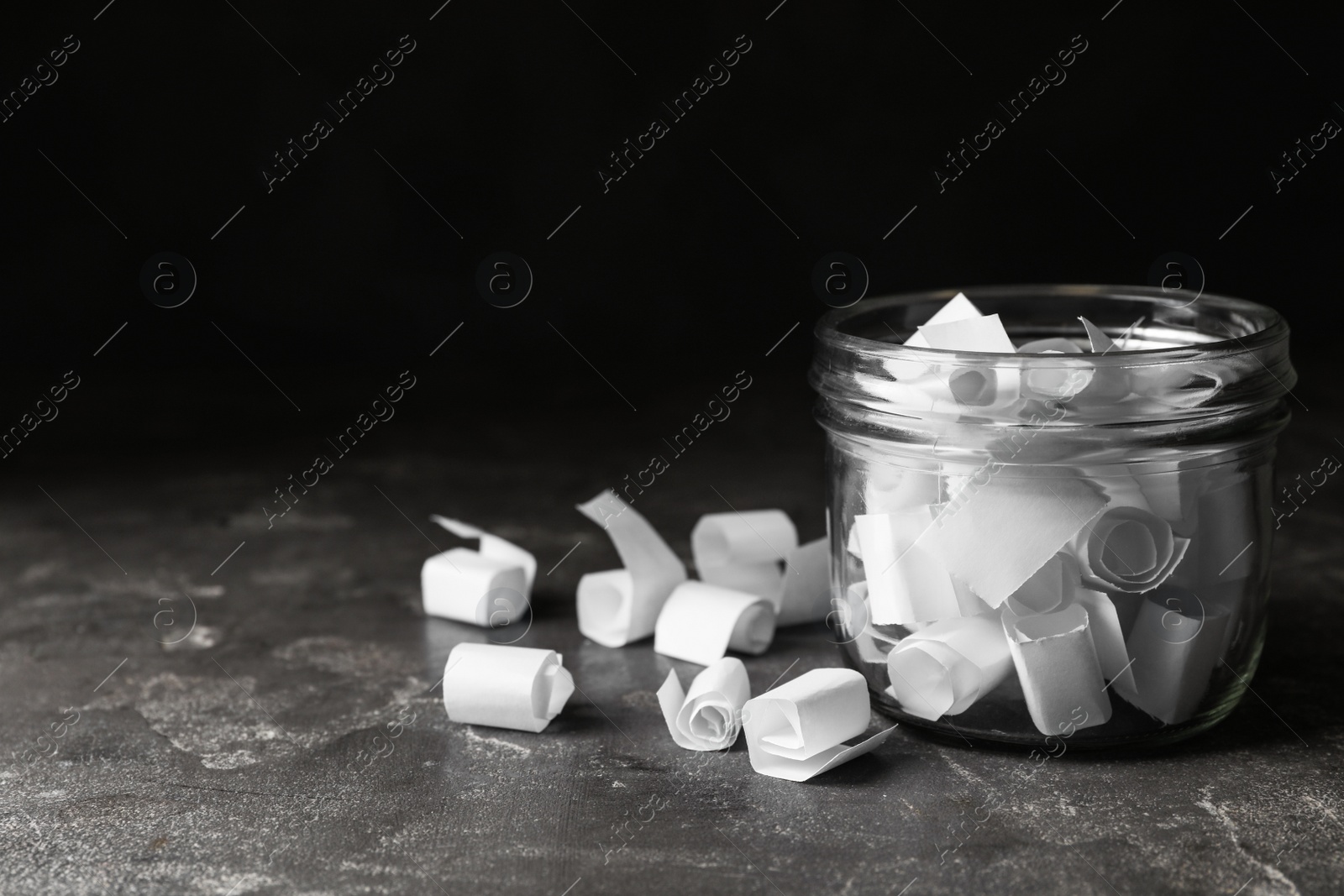 Photo of Glass jar with paper pieces on grey table, space for text