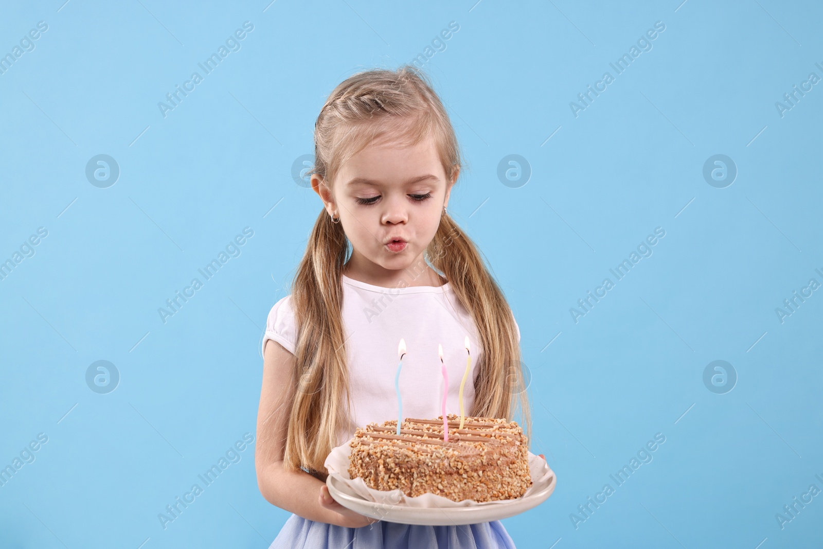 Photo of Birthday celebration. Cute little girl holding tasty cake with burning candles on light blue background