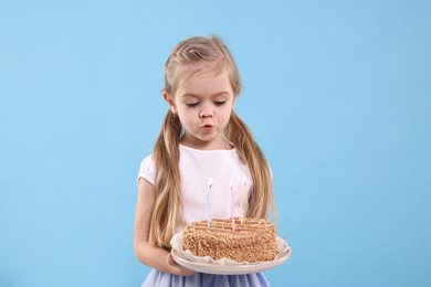 Photo of Birthday celebration. Cute little girl holding tasty cake with burning candles on light blue background