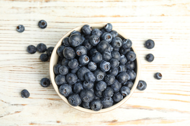 Photo of Tasty ripe blueberries in bowl on white wooden table, flat lay