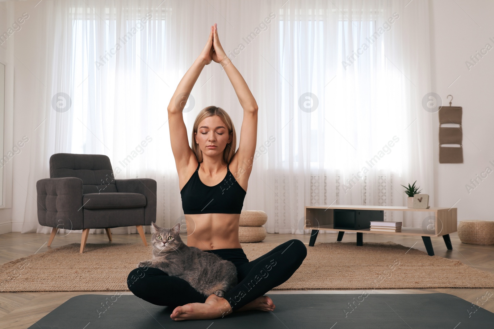 Photo of Beautiful woman with cat practicing yoga at home