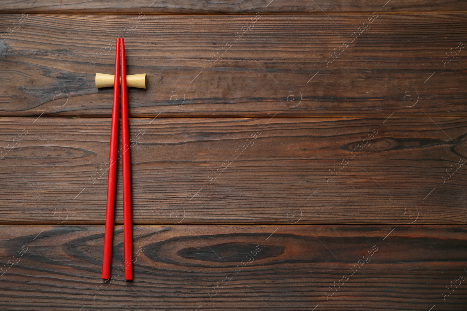 Photo of Pair of red chopsticks with rest on wooden table, top view. Space for text