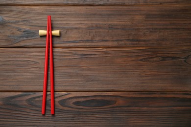 Photo of Pair of red chopsticks with rest on wooden table, top view. Space for text