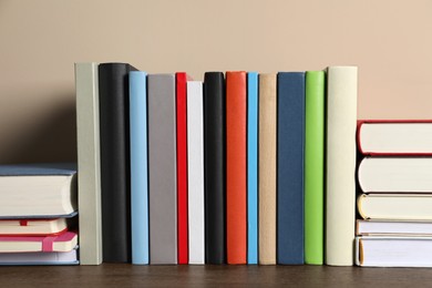 Photo of Many different hardcover books on wooden table near beige wall