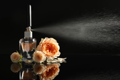 Photo of Beautiful flowers, elegant bottle and spray of perfume on black background