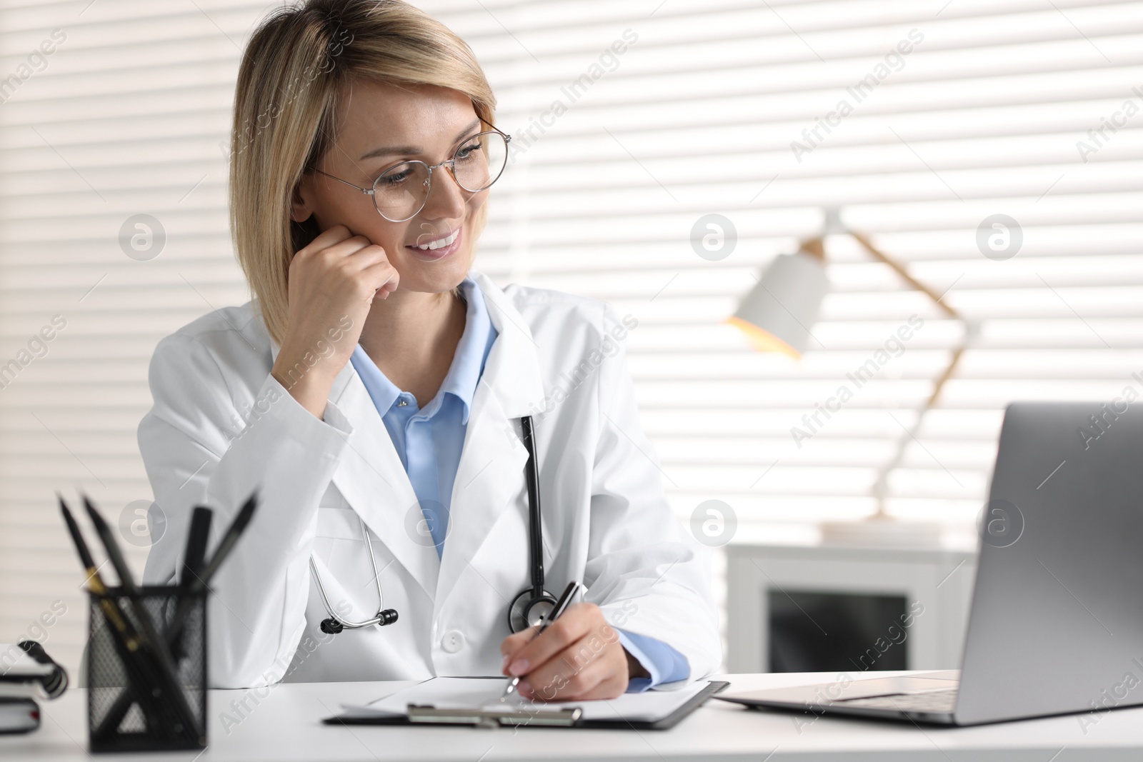 Photo of Smiling doctor with laptop having online consultation at table in office