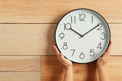 Woman touching clock on wooden wall, space for text. Time management