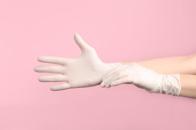 Person putting on medical gloves against pink background, closeup of hands