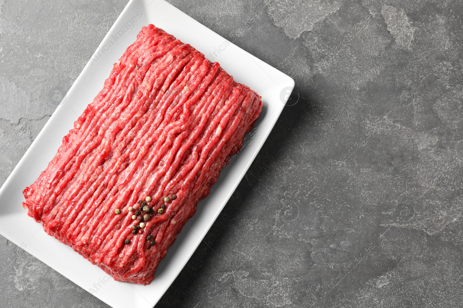 Photo of Raw ground meat and peppercorns on grey table, top view. Space for text